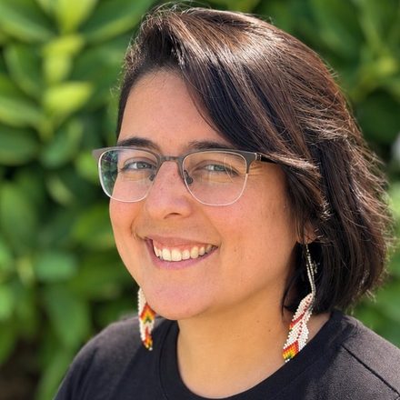 Kim González-Chang smiling outdoors in front of green leaves